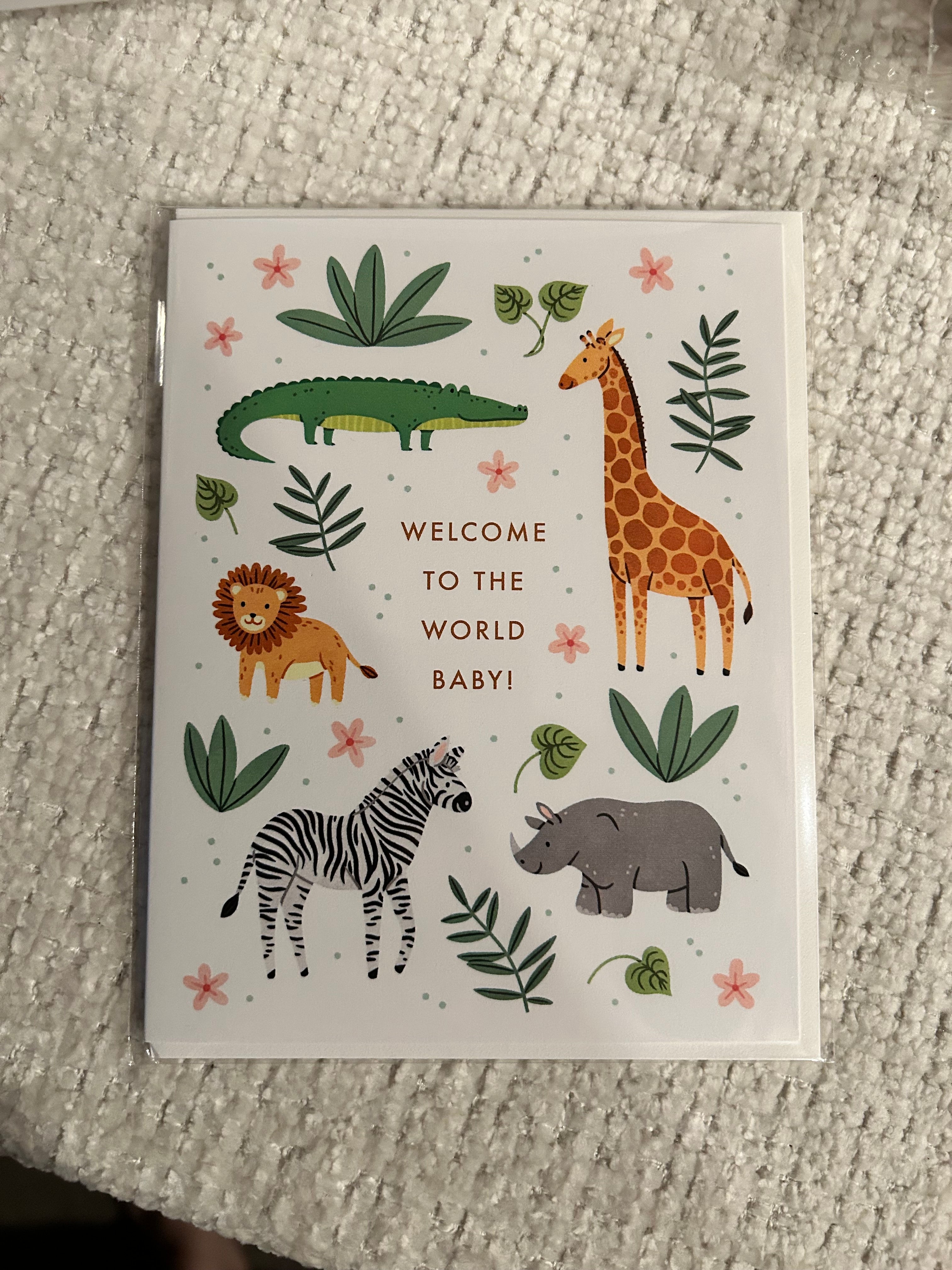 Gender-neutral baby greeting card featuring adorable safari animals including a giraffe, lion, zebra, crocodile, and rhino with greenery and the words "Welcome to the World Baby!"