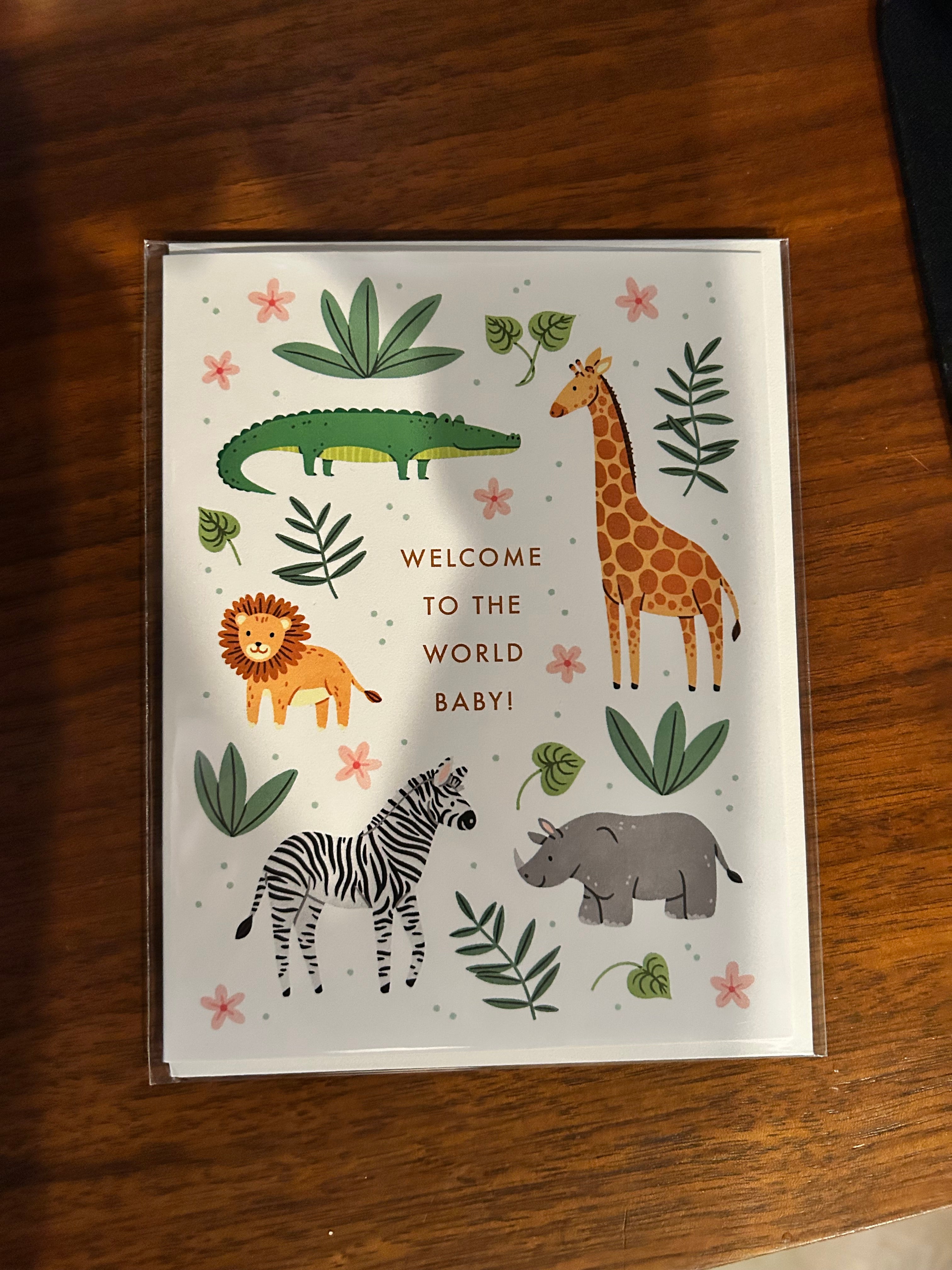 Gender-neutral baby greeting card featuring adorable safari animals including a giraffe, lion, zebra, crocodile, and rhino with greenery and the words "Welcome to the World Baby!"