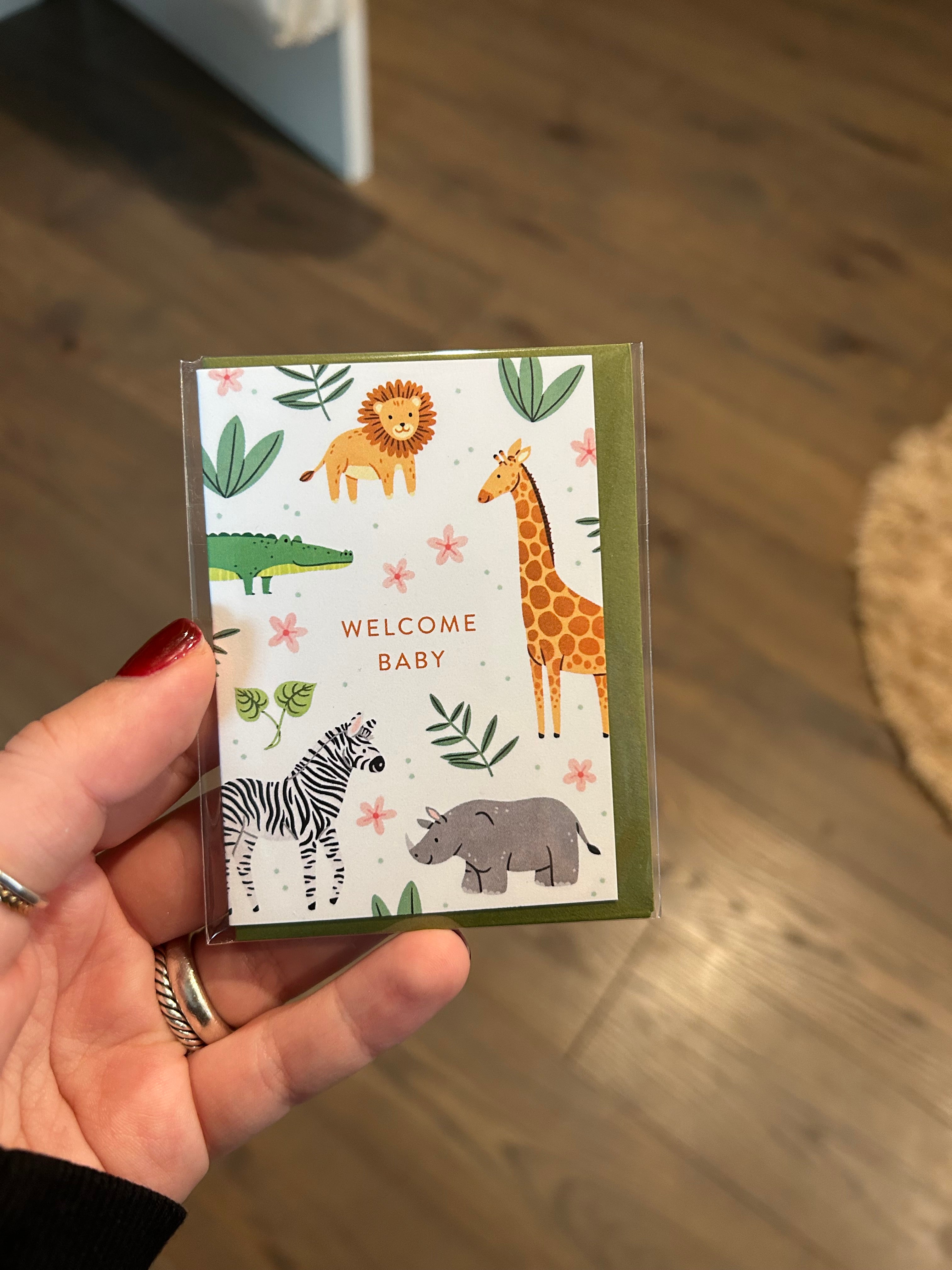 Mini greeting card featuring adorable safari animals including a lion, giraffe, zebra, rhinoceros, and crocodile surrounding the words "Welcome Baby."
