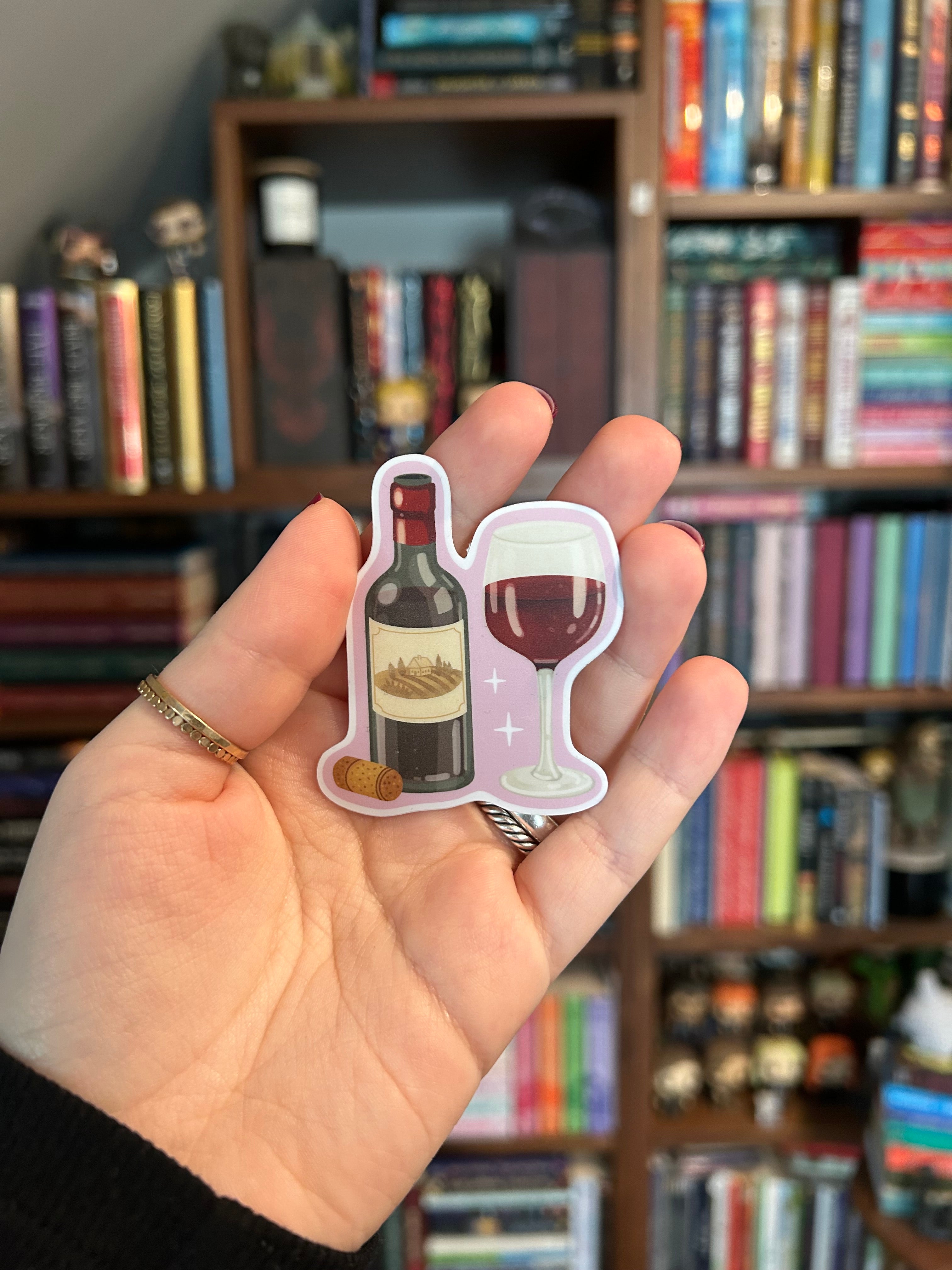 Waterproof vinyl sticker featuring a bottle of red wine, a filled wine glass, and a cork on a soft pink background.