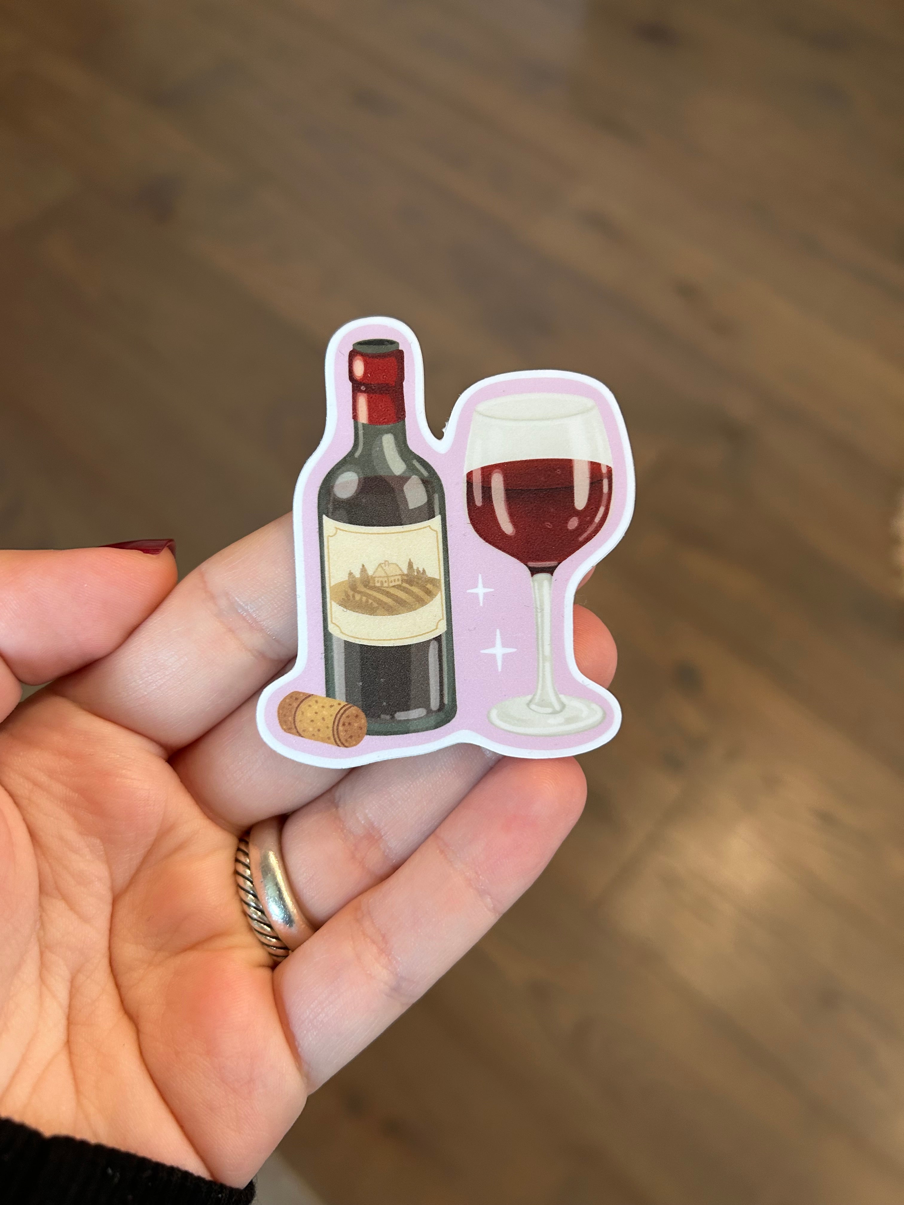 Waterproof vinyl sticker featuring a bottle of red wine, a filled wine glass, and a cork on a soft pink background.