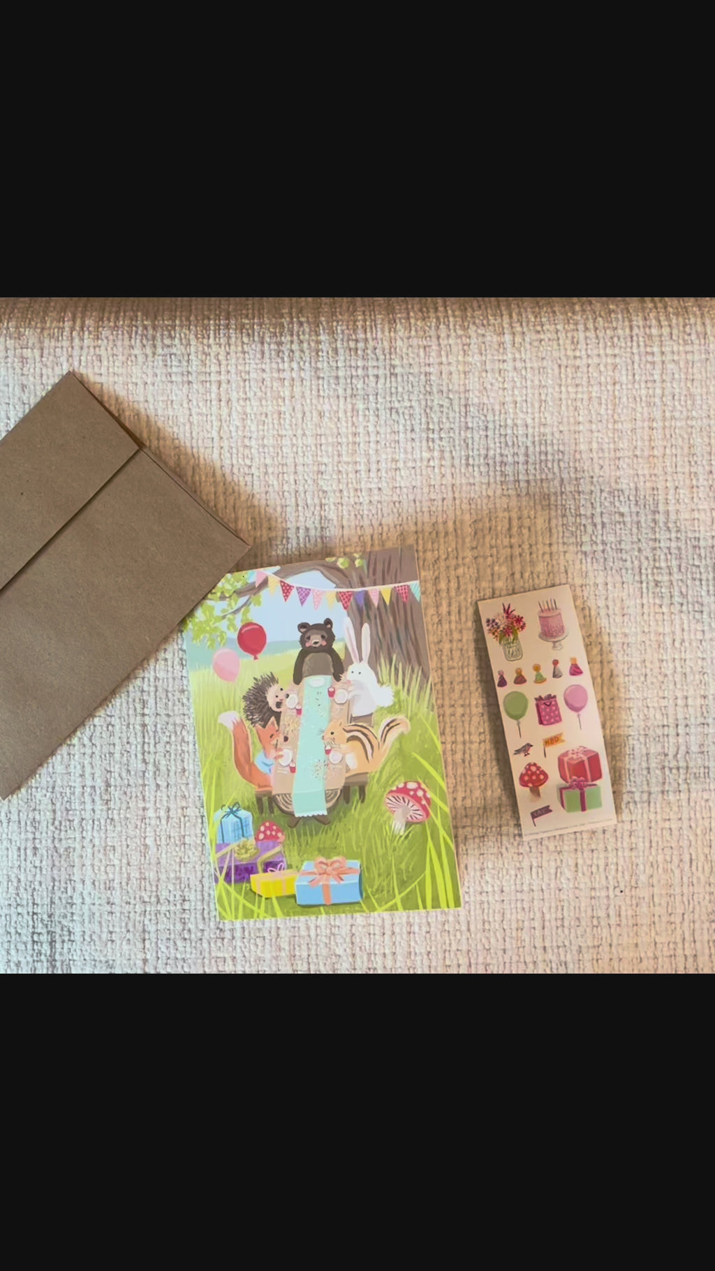 Video of woodland birthday greeting card featuring a bear, bunny, hedgehog, squirrel, and chipmunk celebrating at a picnic with balloons, presents, and a matching birthday sticker sheet.
